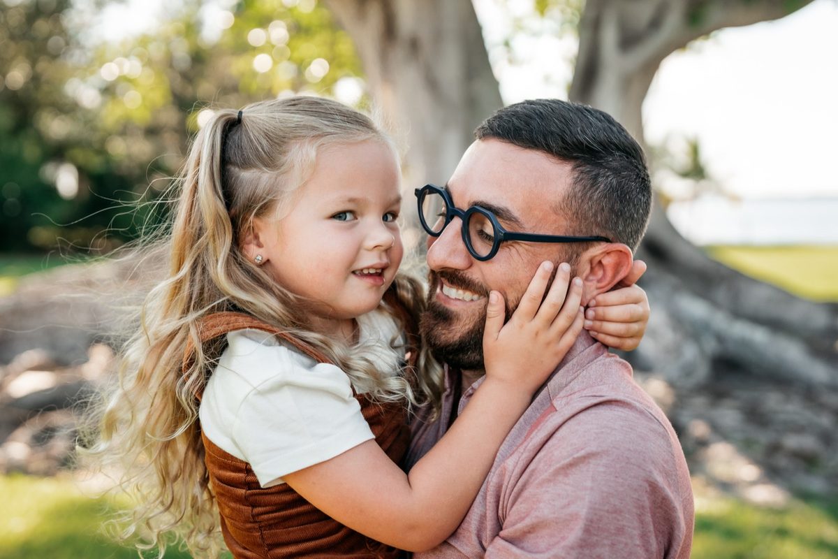 Co-founder Allen smiling cheek-to-cheek with his daughter Isla outdoors under a large tree